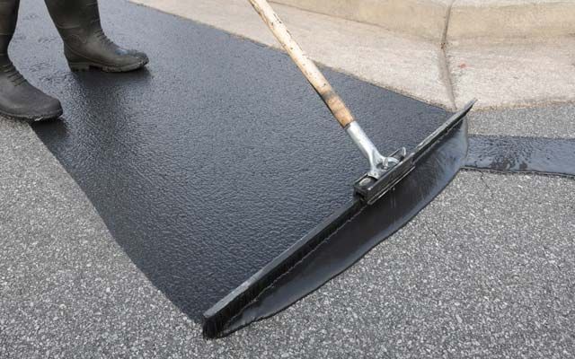 Fresh asphalt sealcoat being applied with a squeegee to a tar surface